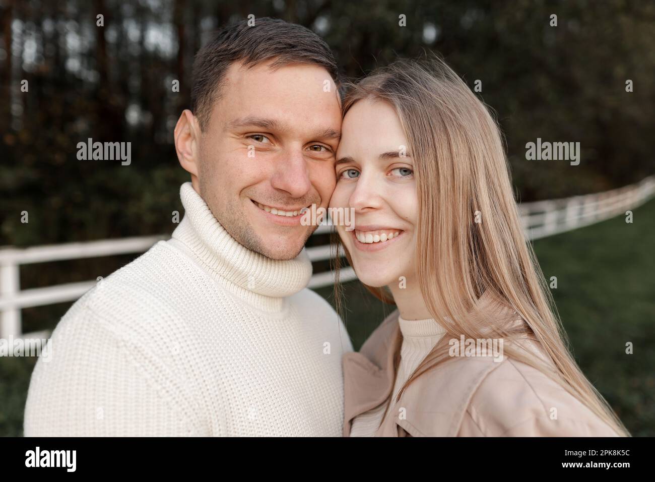 Ein junges, glückliches, romantisches schwangeres Paar geht an warmen Herbsttagen mit Händchen nach draußen. Schwangere Frau in Strickkleid und ihr gutaussehender Mann erwarten Stockfoto