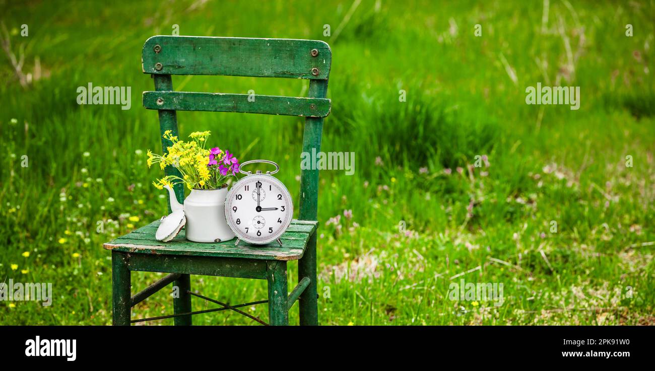 Stuhl, Blumenstrauß, Wecker, Ziffernblatt mit drei Uhr, Symbol für Zeitumstellung auf Sommerzeit Stockfoto