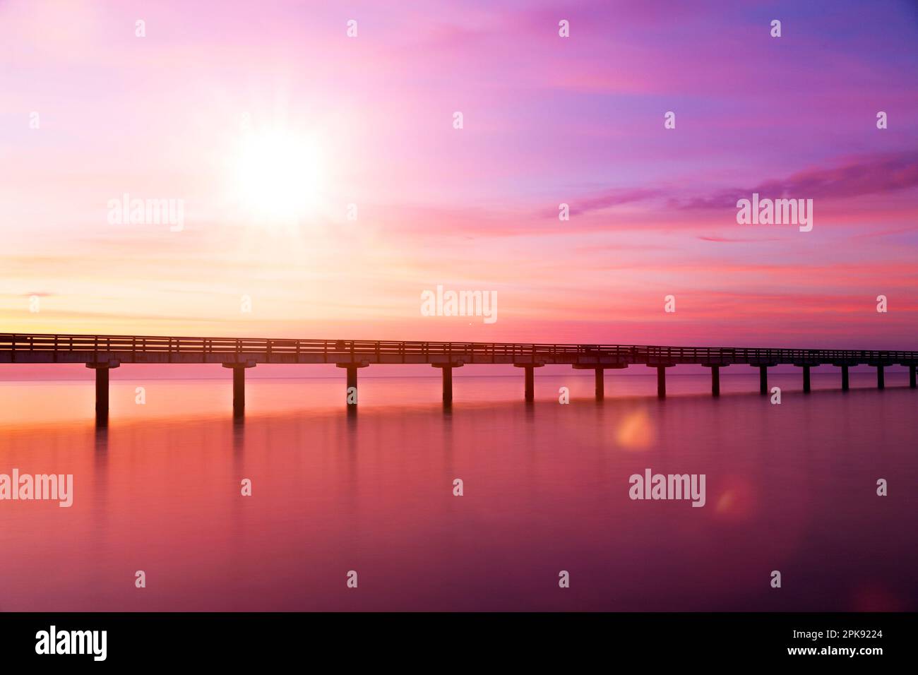 Brücke über Wasser bei Sonnenaufgang in lilafarbener Stimmung Stockfoto