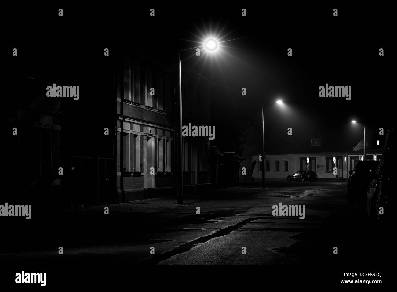 Nachts auf der Straße, kleiner Nebel in der Laterne, Autos parken am Straßenrand, Schwarzweiß-Fotografie Stockfoto