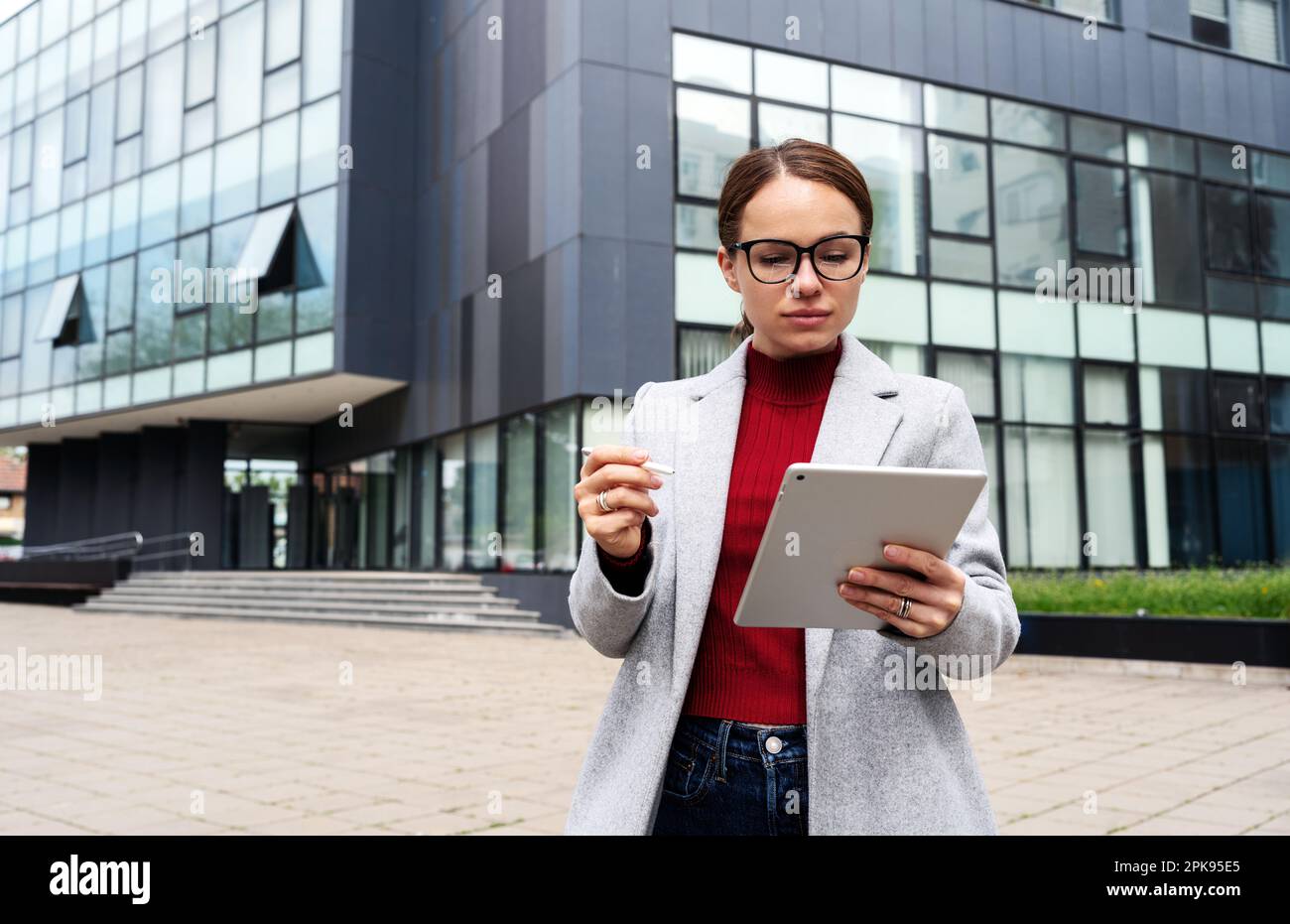 Geschäftsfrau mit Brille, die im Freien an ihrem digitalen Tablet arbeitet, gegen ein Business Center. Stockfoto