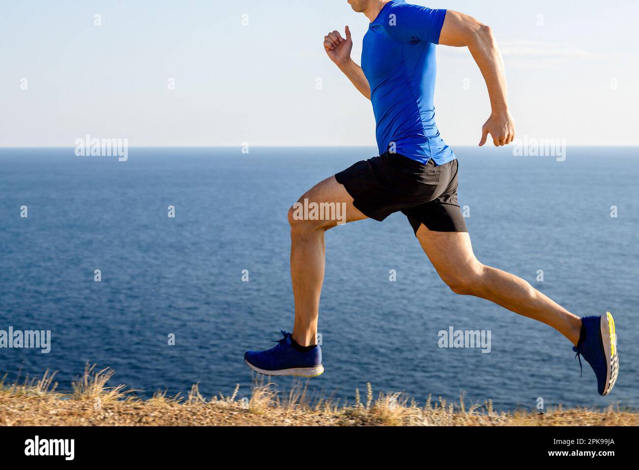 Männlicher Läufer, der im Hintergrund von Meer und Himmel Bergwandern kann, joggt im Sommer entlang der Küste Stockfoto