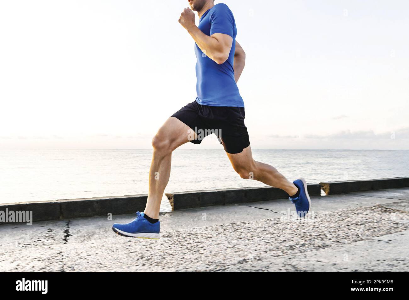 Muskulöser männlicher Läufer, der morgens im Morgengrauen am Ufer läuft, joggt im Sommer an der Küste entlang Stockfoto
