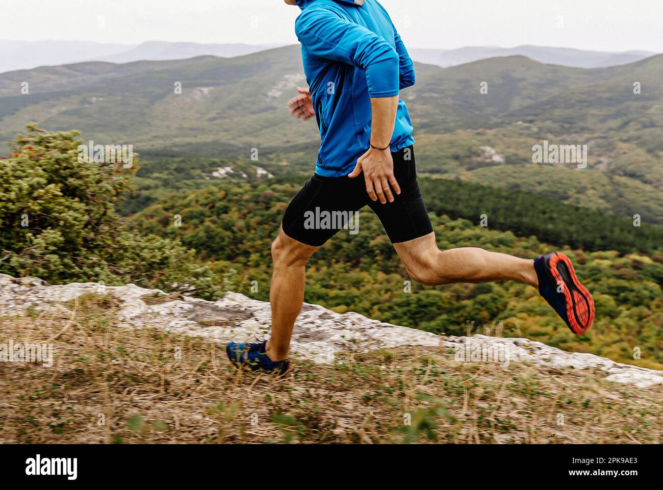 Männlicher Läufer in Windjacke und Strumpfhosen, der am Abgrund läuft, männlicher Jogger-Athlet, der Bergpfad läuft Stockfoto