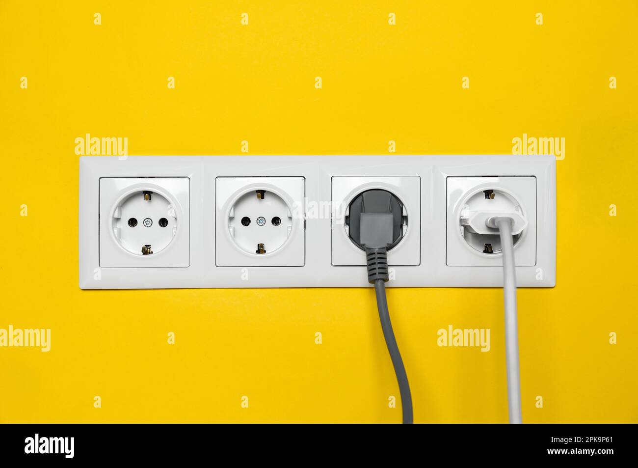 Steckdosen mit eingesteckten Steckern an der gelben Wand. Stromversorgung  Stockfotografie - Alamy