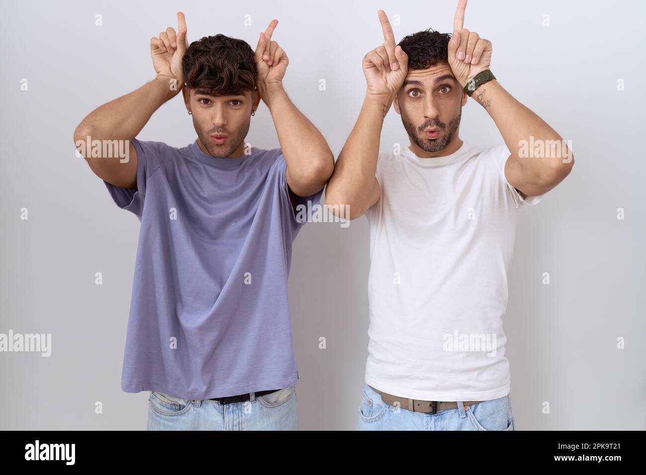 Homosexuelles schwules Paar, das über weißem Hintergrund steht und lustige Geste macht, mit dem Finger über dem Kopf wie Bullenhörner Stockfoto