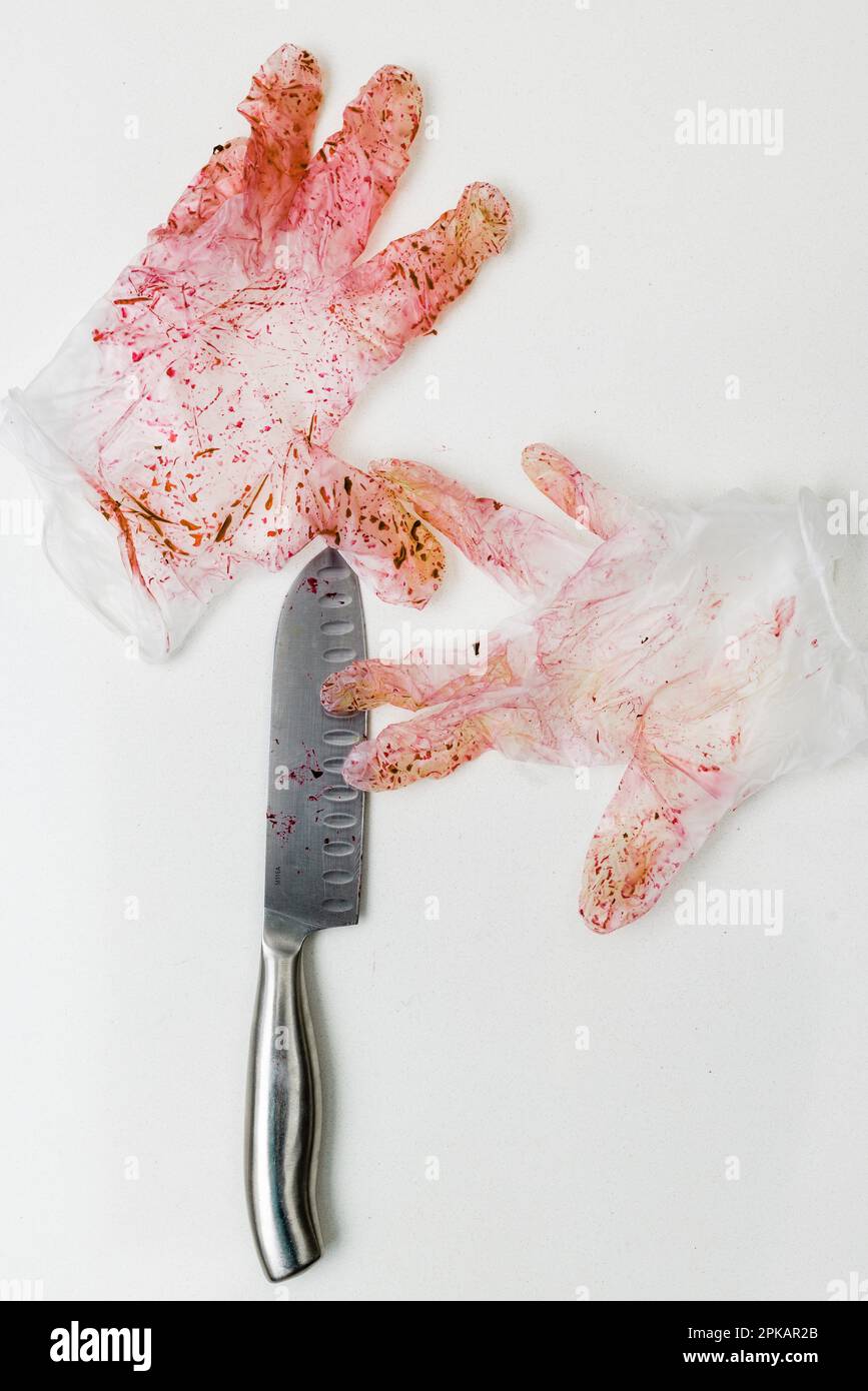 Rot verfärbtes Paar Einweghandschuhe mit Messer auf einer weißen Oberfläche Stockfoto