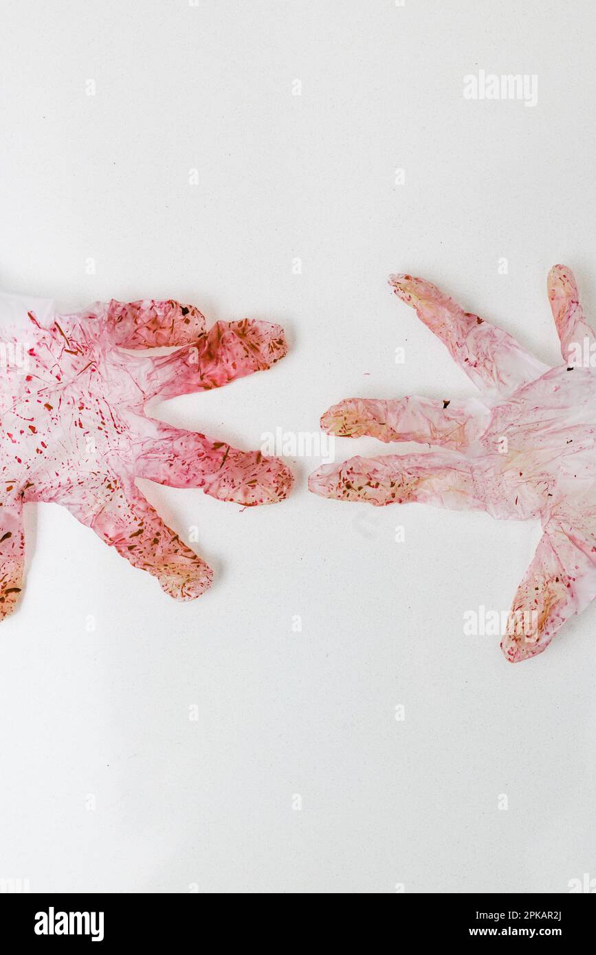 Rot verfärbtes Paar Einweghandschuhe auf einer weißen Oberfläche Stockfoto