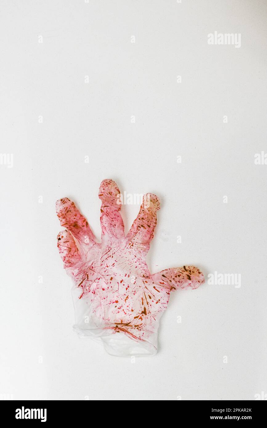 Einzelner roter verfärbter Einweghandschuh auf einer weißen Oberfläche Stockfoto