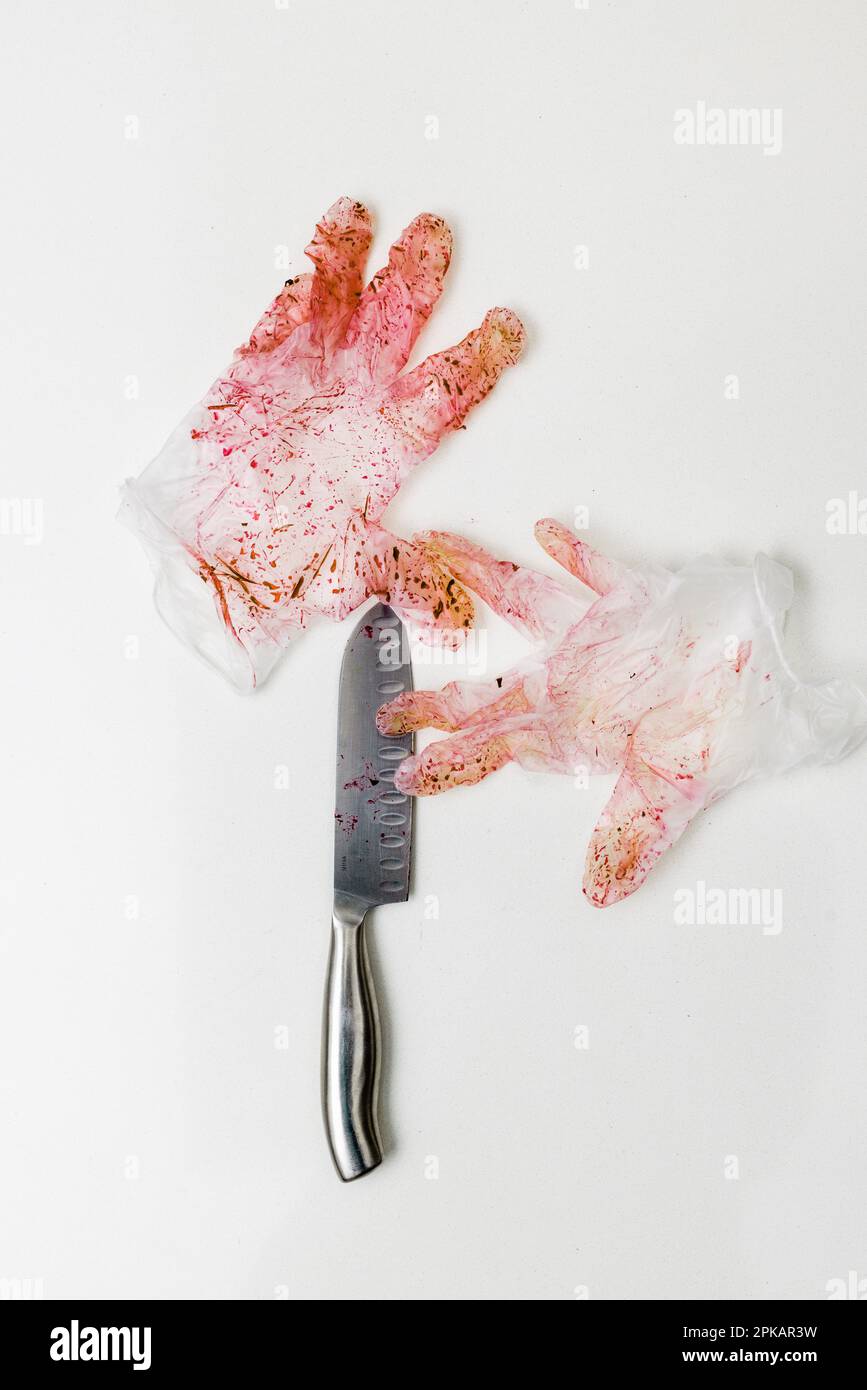 Rot verfärbtes Paar Einweghandschuhe mit Messer auf einer weißen Oberfläche Stockfoto