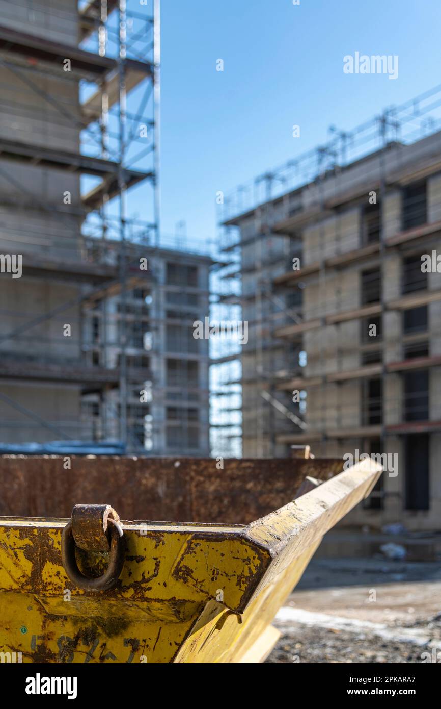 Ein gelber Behälter für Bauabfälle steht auf einer Baustelle vor Gerüstbauten im Hintergrund Stockfoto