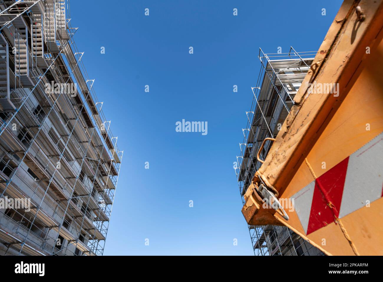 Ungewöhnliche Perspektive beim Schneiden eines Orangenabfallbehälters auf einer Baustelle mit zwei im Hintergrund im Bau befindlichen Gebäuden Stockfoto