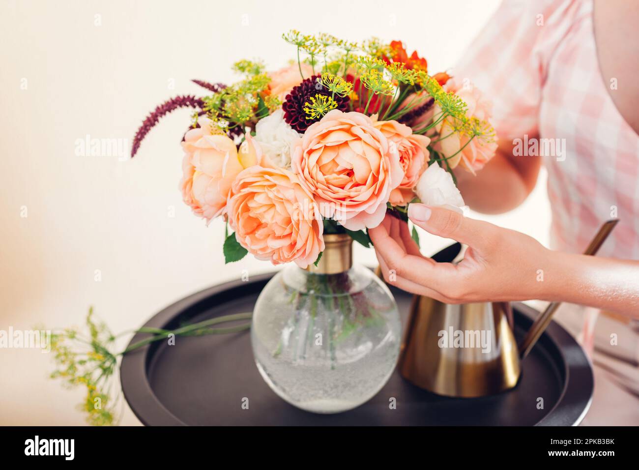Nahaufnahme von frischen englischen Rosen Lady of Shallott. Frau macht Blumenstrauß in Vase mit orange roten Blumen mit Grün auf dem Tisch zu Hause. Stockfoto