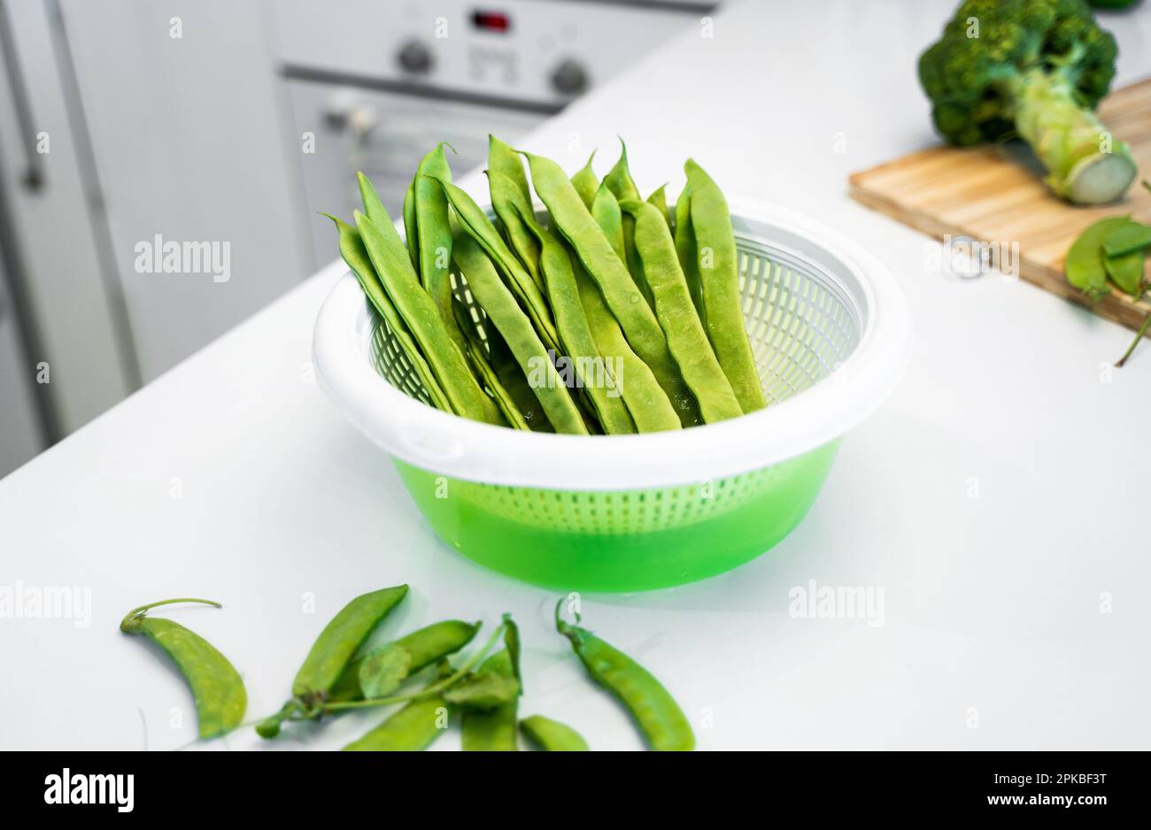 Grünes Gemüse, romano-Helda-Bohnen, grüne Erbsen und Brokkoli auf dem Holzbrett. Weißer Küchentisch zu Hause. Das Konzept einer gesunden Ernährung Stockfoto