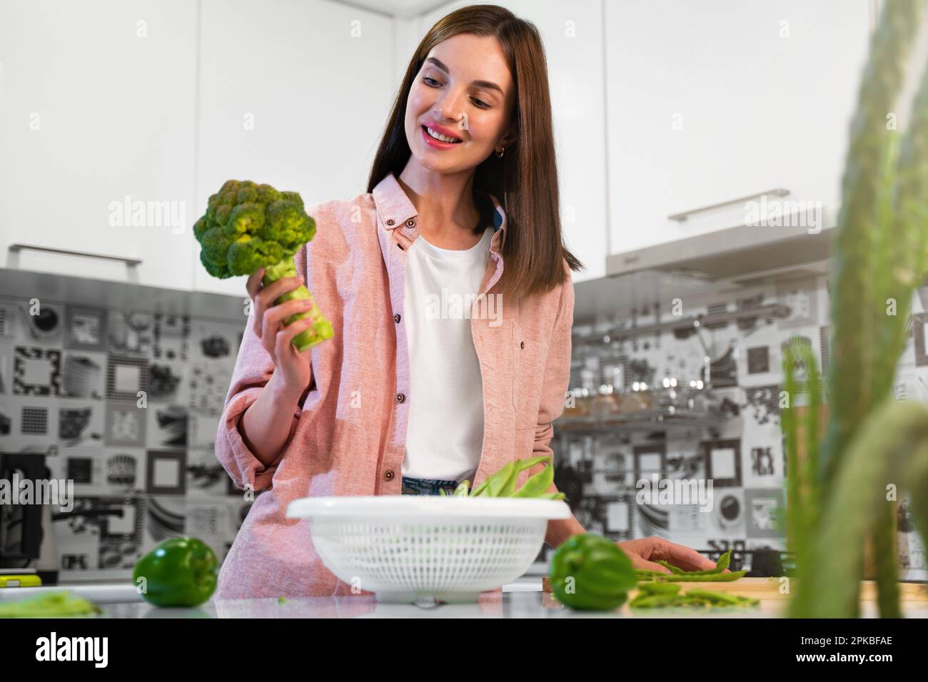 Eine junge Frau steht in der Küche, hält Brokkoli in den Händen und kocht einen vegetarischen Diätsalat. Das Konzept einer gesunden Ernährung Stockfoto