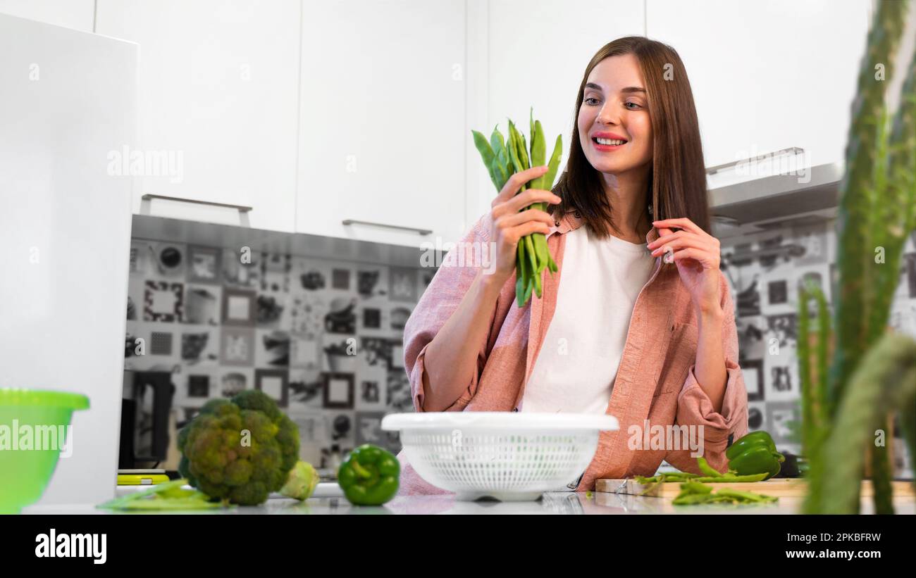 Eine junge, lächelnde, schöne Frau, die die grünen Bohnen von romano Helda in den Händen hält. Das Konzept einer gesunden Ernährung, Hausmannskost und vegetarischer Ernährung. Stockfoto