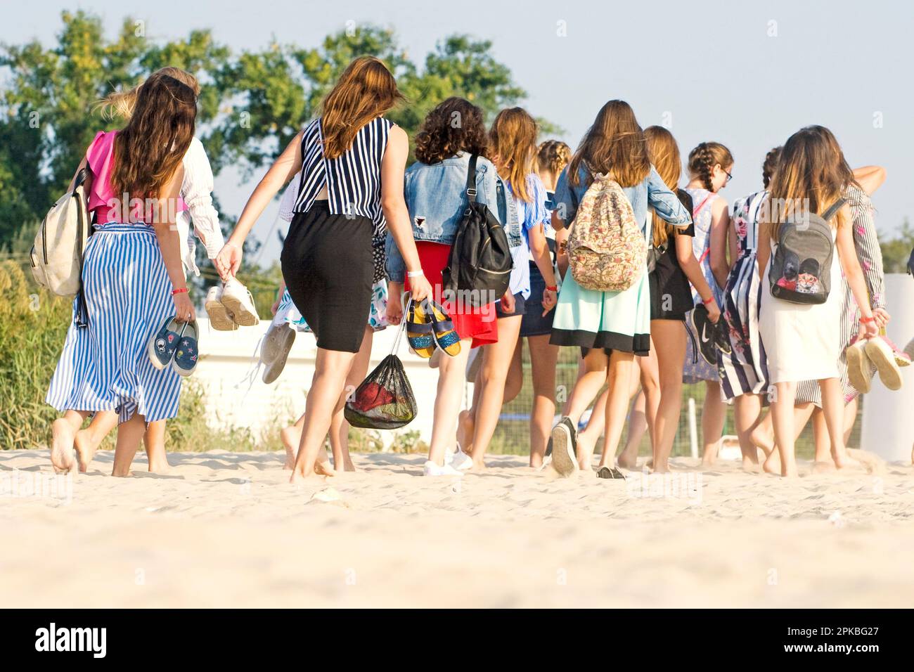 Touristen von hinten gehen barfuß in der Sonne am Strand entlang Stockfoto