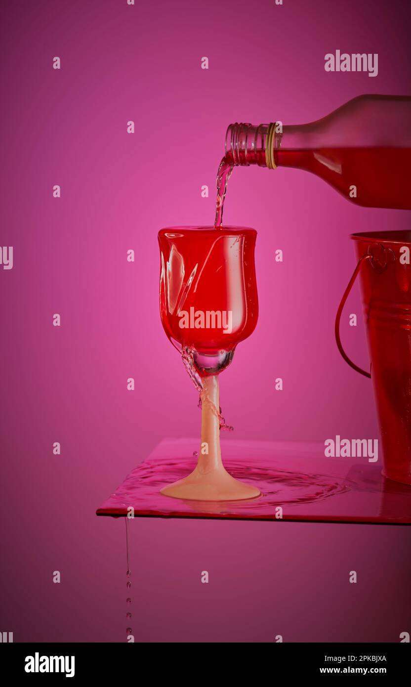 Eine Flasche Alkohol wird in ein Glas gegossen, wobei das Glas überläuft und das Getränk um es herum spritzt. Stockfoto