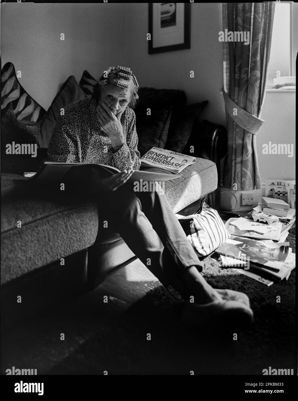 Schwarz-weiß-Bild einer älteren Frau, erschrocken und in die Kamera blickend, hat sie Rollers im Haar und liest Zeitungen Stockfoto
