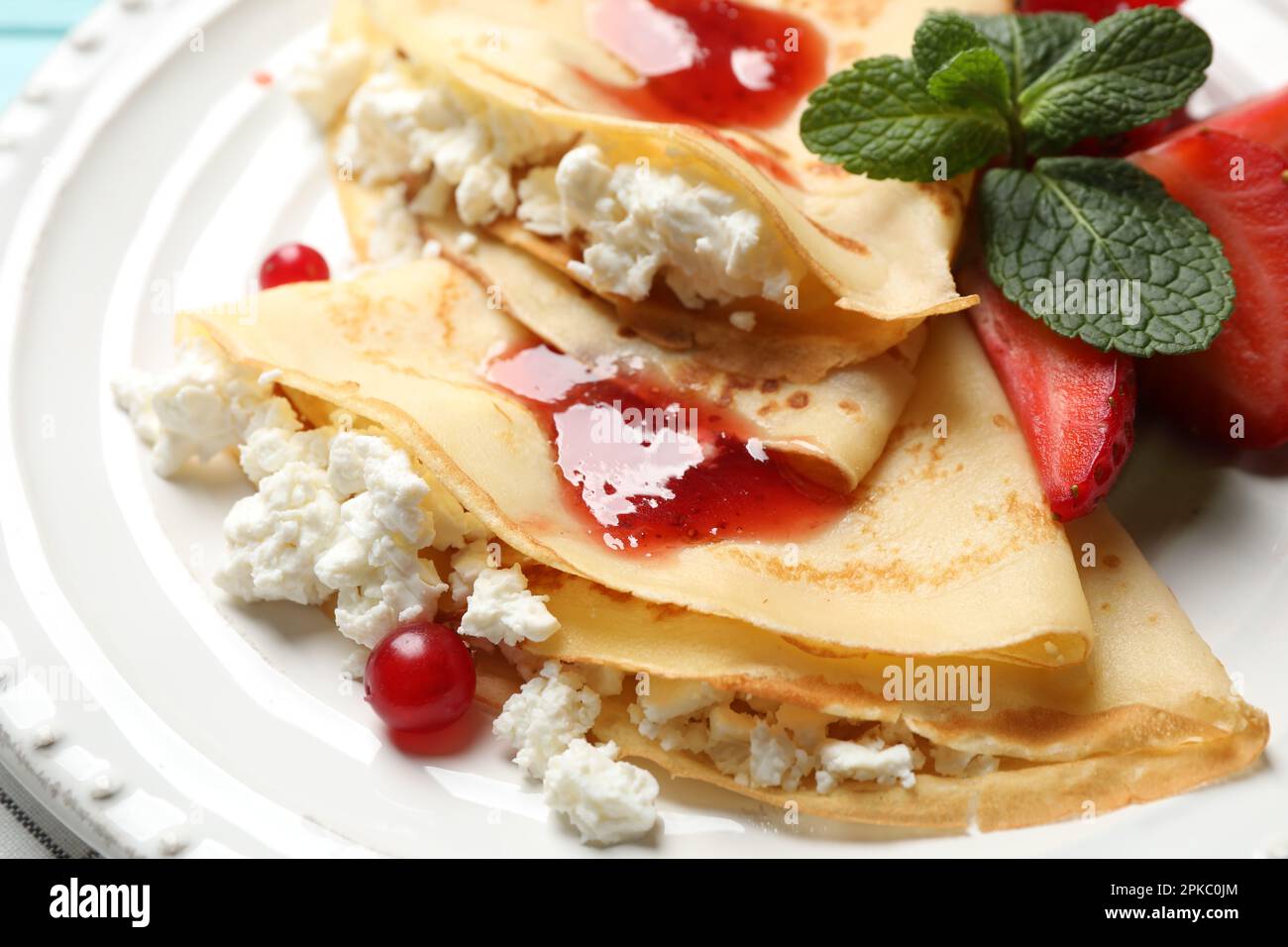 Leckere dünne Pfannkuchen mit Hüttenkäse und Marmelade auf dem Teller, Nahaufnahme Stockfoto