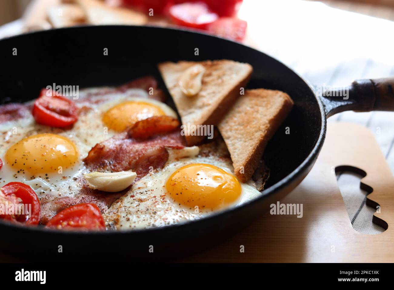 Leckere Spiegeleier mit Speck und Tomaten in der Pfanne, Nahaufnahme Stockfoto