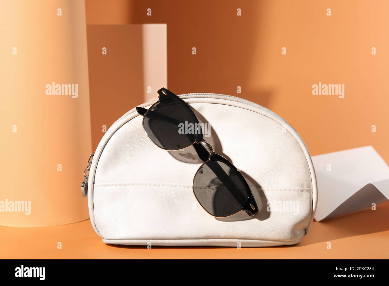 Stilvolle Sonnenbrille und weiße Make-up-Tasche auf hellorangefarbenem Hintergrund Stockfoto