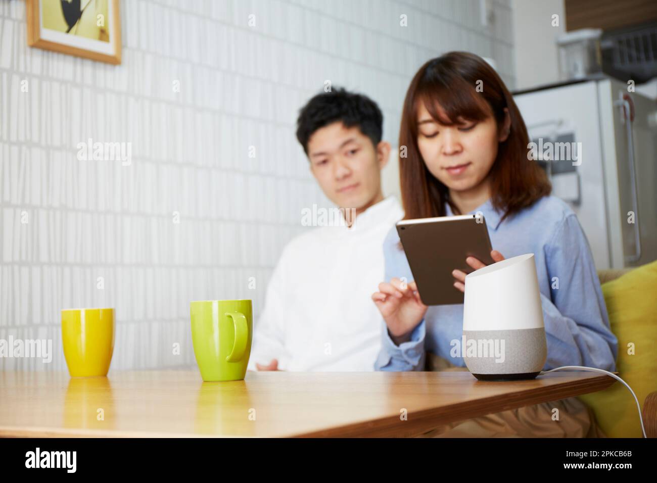 Mann und Frau entspannen sich im Wohnzimmer mit AI-Lautsprechern auf dem Tisch Stockfoto