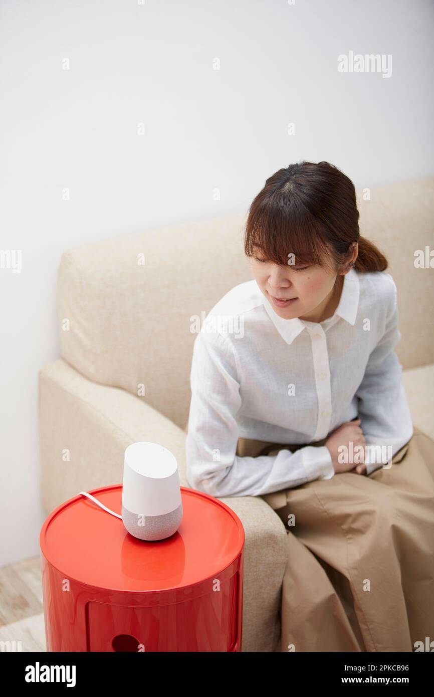 Frau, die auf dem Sofa sitzt und mit dem AI-Lautsprecher spricht Stockfoto