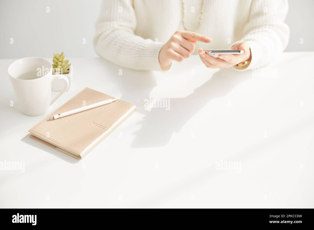 Frau, die ein Smartphone bedient und vor einem Schreibtisch sitzt Stockfoto