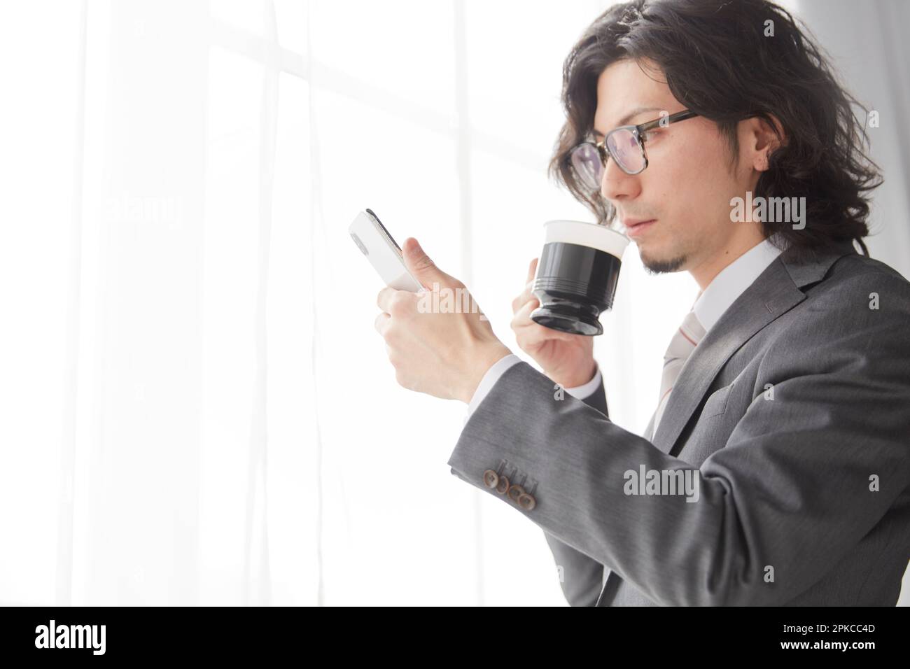 Büroangestellter trinkt Kaffee, während er ein Smartphone bedient Stockfoto