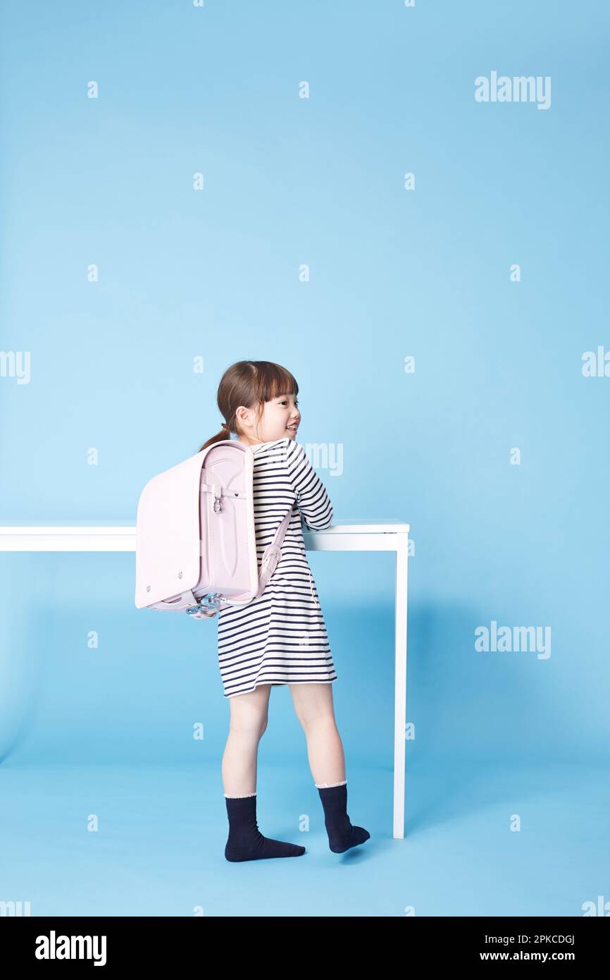 Mädchen mit Schultasche steht vor dem weißen Tisch Stockfoto