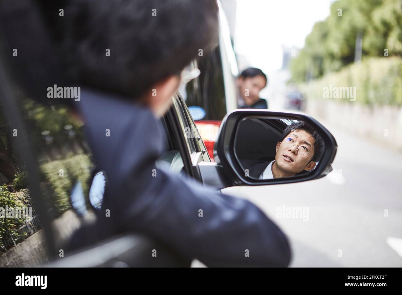 Das Gesicht eines Mannes im Rückspiegel, mit dem Gesicht aus dem Autofenster Stockfoto