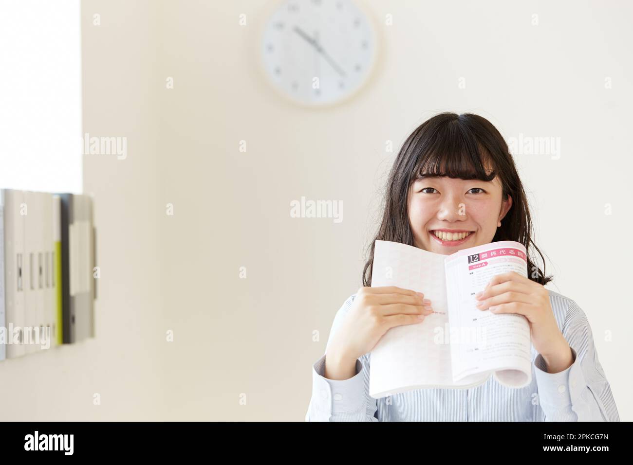 Ein Highschool-Mädchen, das ein Nachschlagewerk hält, mit beiden Händen und lächelnd Stockfoto