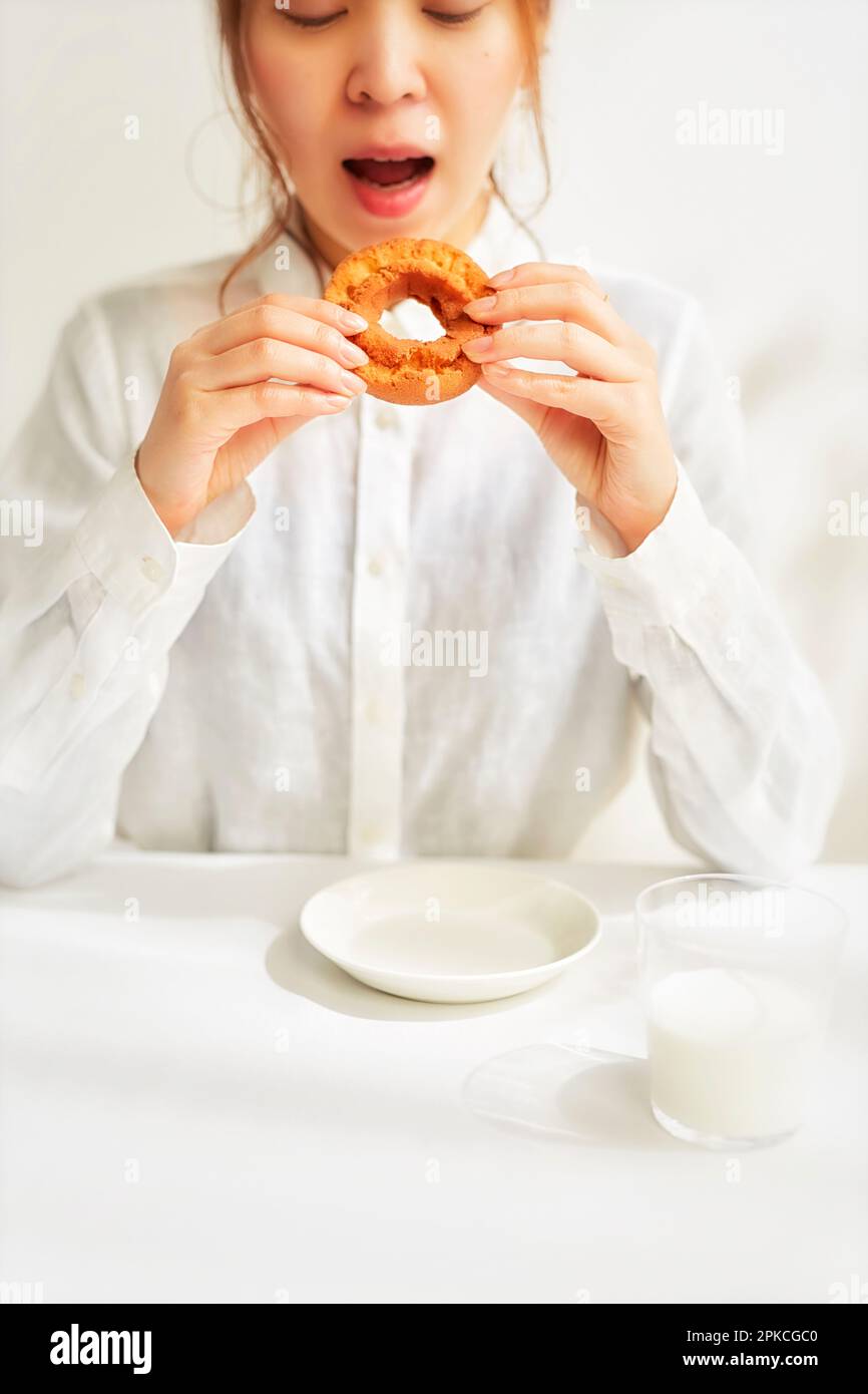 Eine Frau in Weiß isst Donut an einem weißen Tisch im weißen Raum Stockfoto