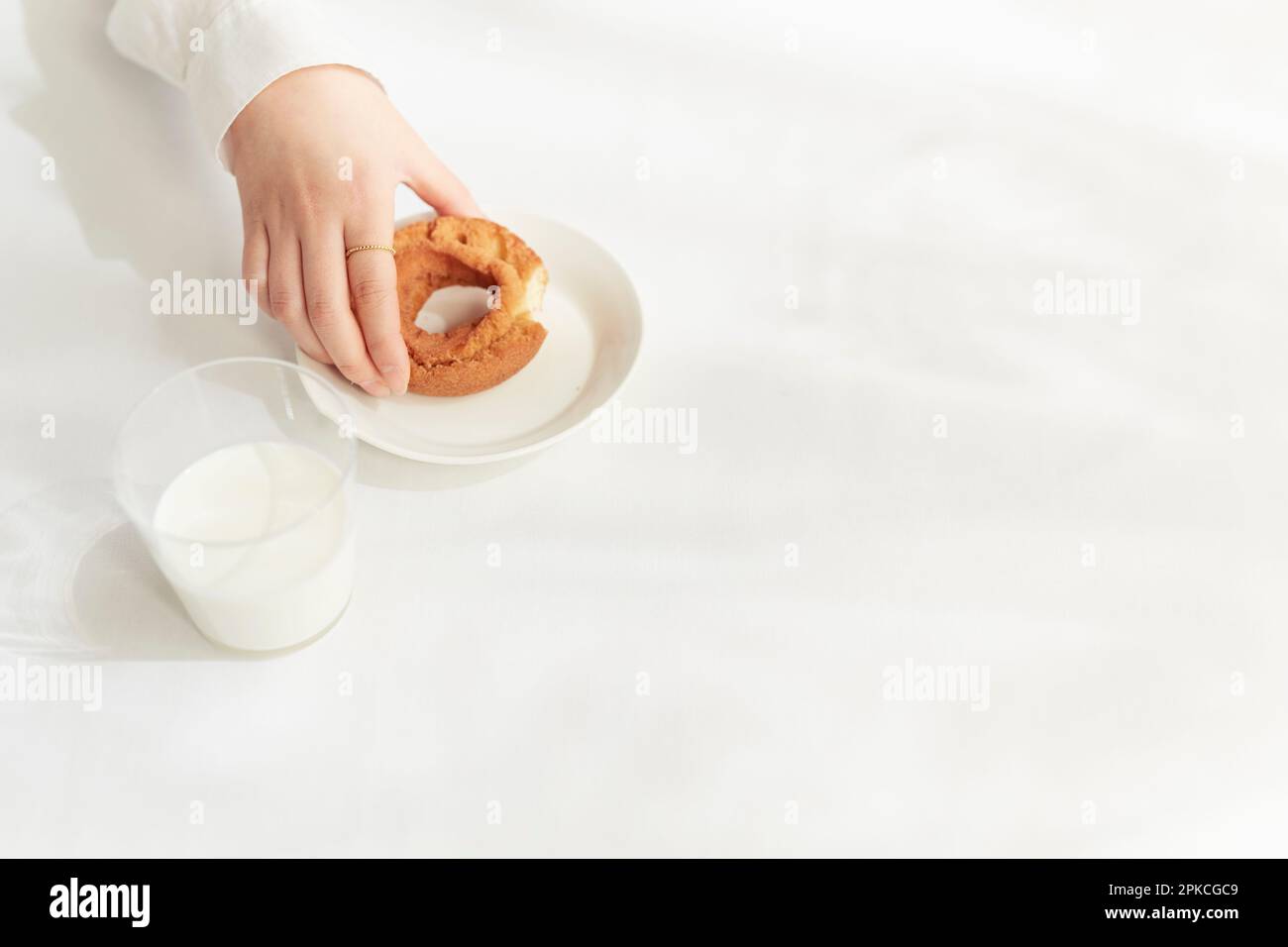 Person in Weiß isst Donut am weißen Tisch Stockfoto