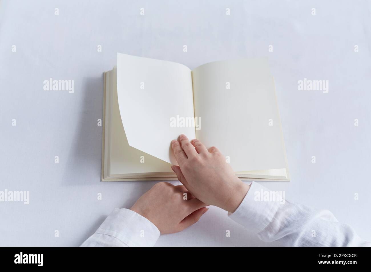 Hand einer Person, die ein leeres Buch an einem weißen Tisch liest Stockfoto