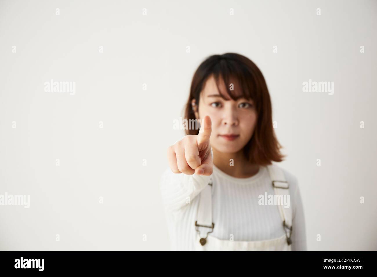 Eine Frau, die mit dem Finger vor eine weiße Wand zeigt Stockfoto