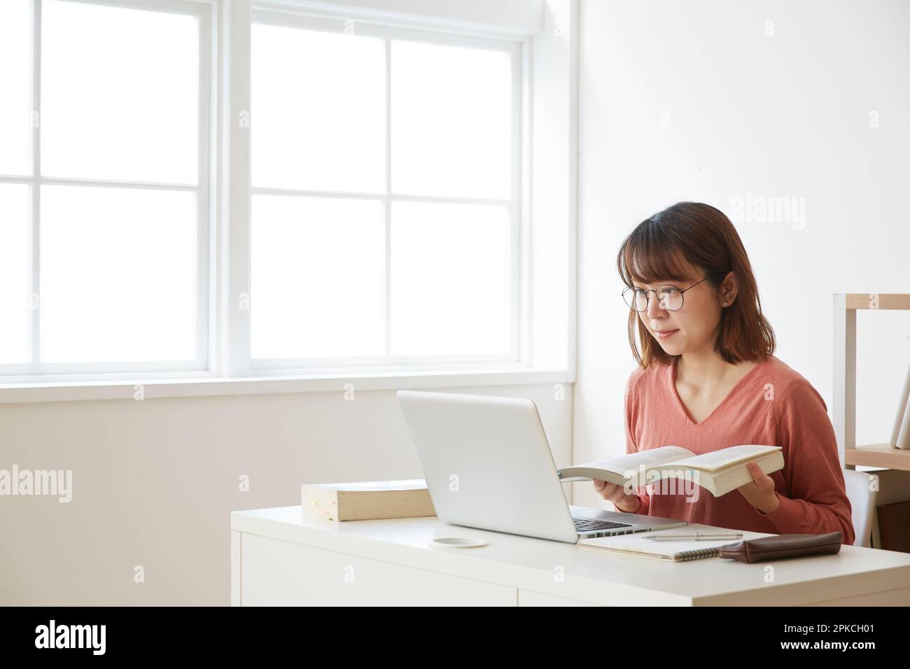 Eine Frau, die an einem Computer lernt, während sie sich ein Nachschlagewerk ansieht Stockfoto