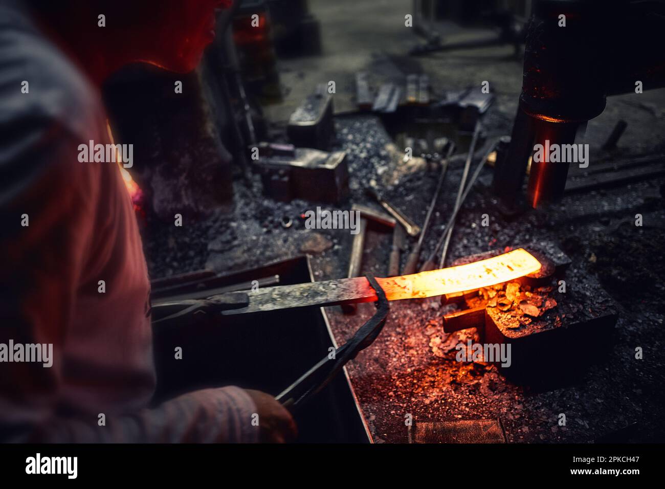 Ein Mann, der mit einem erhitzten roten Eisen in einer Besteckfabrik arbeitet Stockfoto
