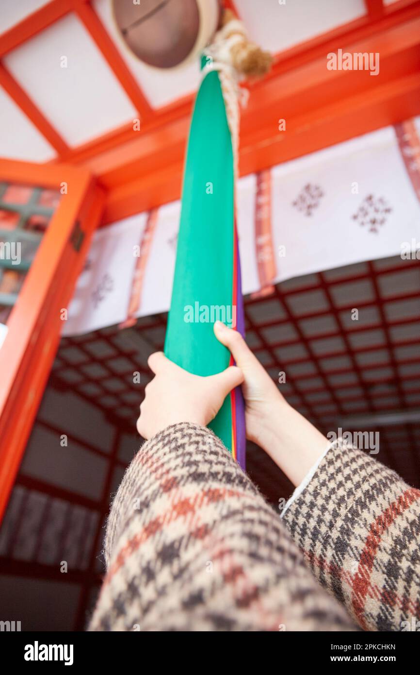 Die Hand einer Frau mit der Hand auf einer Glockenschnur an einem Schrein Stockfoto
