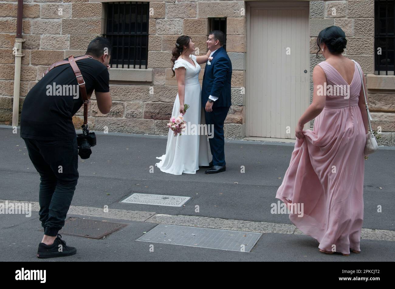 Hochzeitsveranstalter, die ein Fotoshooting für ein asiatisches Paar leiten, wahrscheinlich ausländische Touristen, im The Rocks, Sydney, NSW, Australien Stockfoto