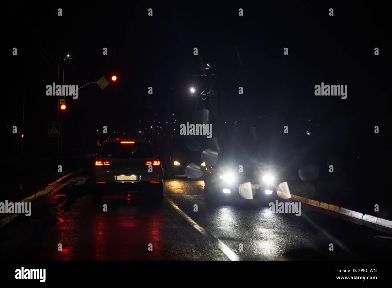 Verkehr auf nasser Straße bei schlechtem Wetter, rote Ampel. Stromausfall in der Ukraine, Krieg Stockfoto