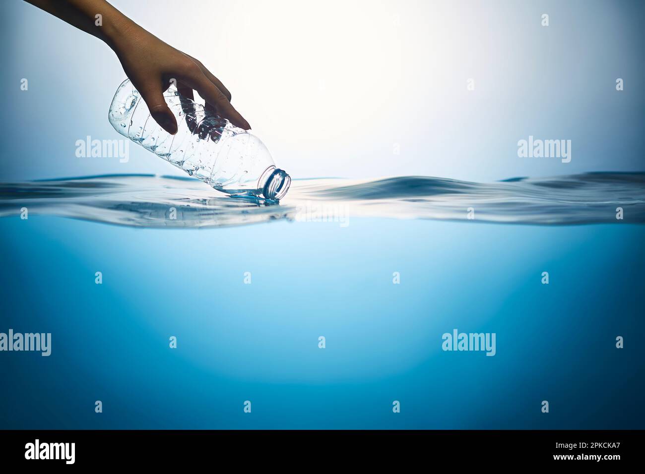 Eine Hand hebt eine Plastikflasche auf, die im Wasser schwimmt Stockfoto