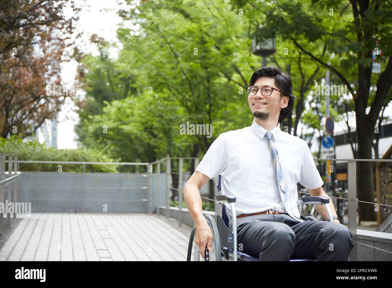 Ein Mann im Rollstuhl lächelt, während er die Rampe hinuntergeht Stockfoto
