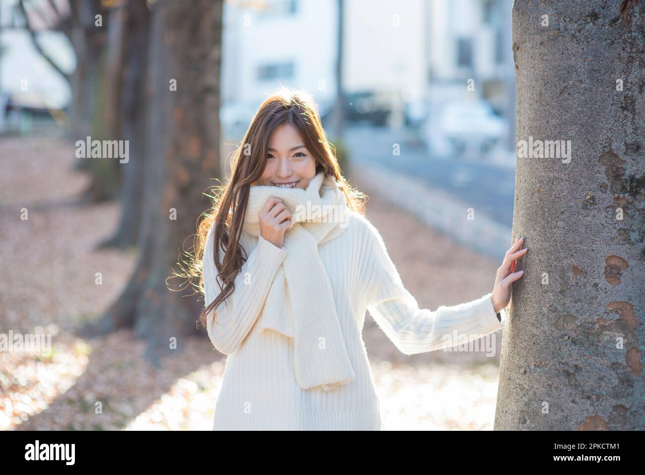 Eine Frau in ihren 20s, die im Winter vor einem Baum in einem Park steht Stockfoto