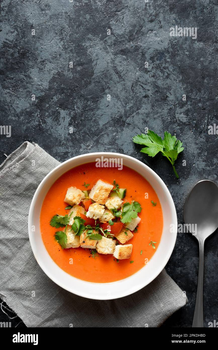 Tomaten-Gazpacho-Suppe mit Croutons in der Schüssel auf dunklem Steinhintergrund mit freiem Textbereich. Kalte Sommersuppe. Draufsicht, flach liegend Stockfoto