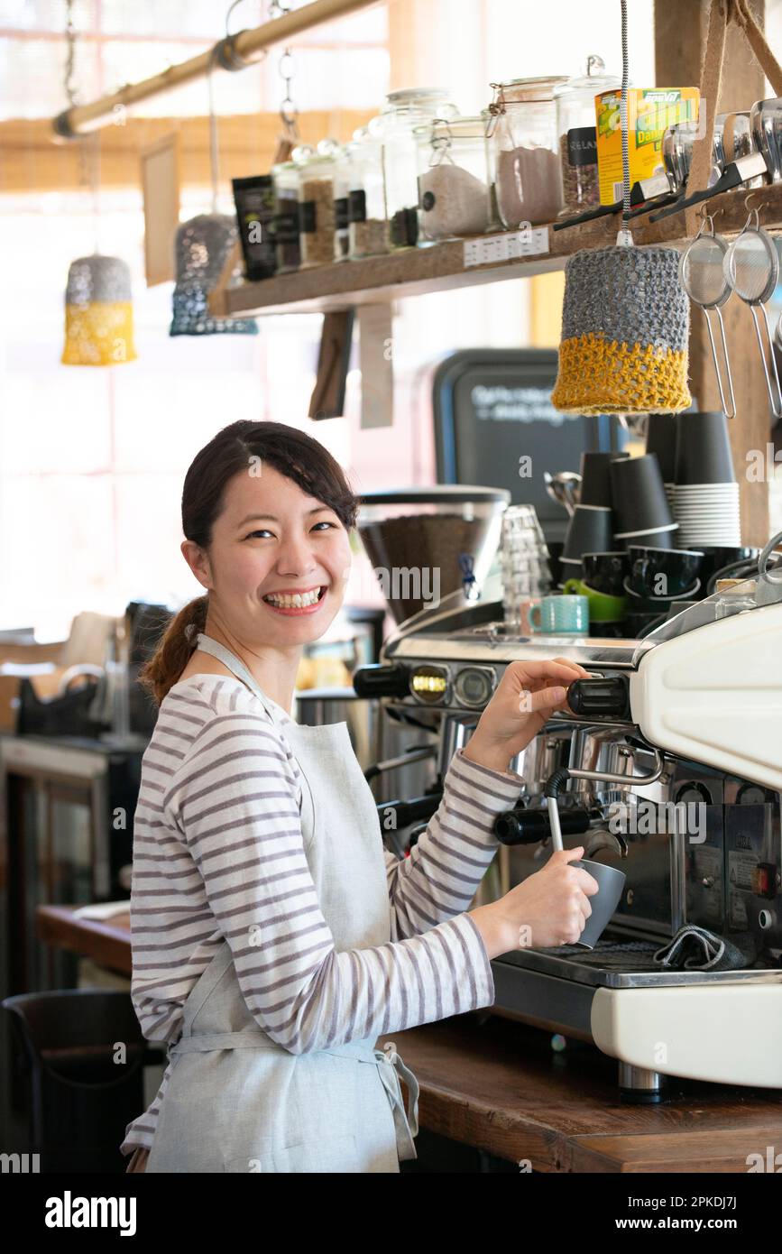 Eine Frau, die in einem Geschäft arbeitet und eine Espressomaschine mit einem Lächeln berührt. Stockfoto