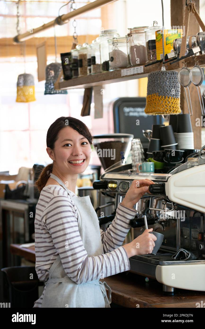 Die Frau des Verkäufers berührte die Espressomaschine mit einem Lächeln Stockfoto