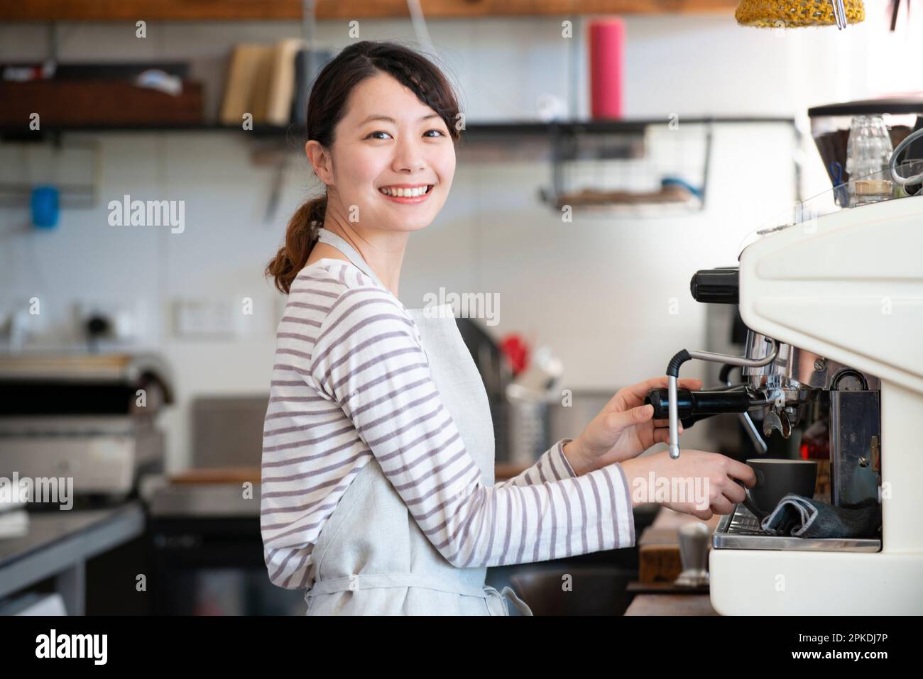 Eine Frau, die in einem Geschäft arbeitet und eine Espressomaschine mit einem Lächeln berührt Stockfoto