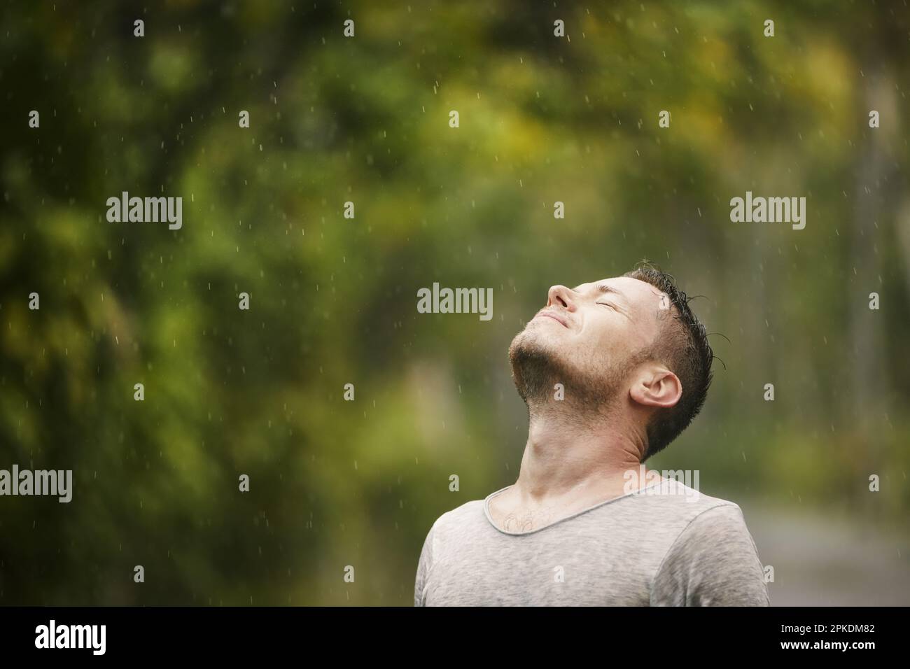 Porträt des Menschen in nassen Kleidern mit geschlossenen Augen bei starkem Regen in der Natur. Themen des Lebens Wasser, Wetter und Umwelt. Stockfoto